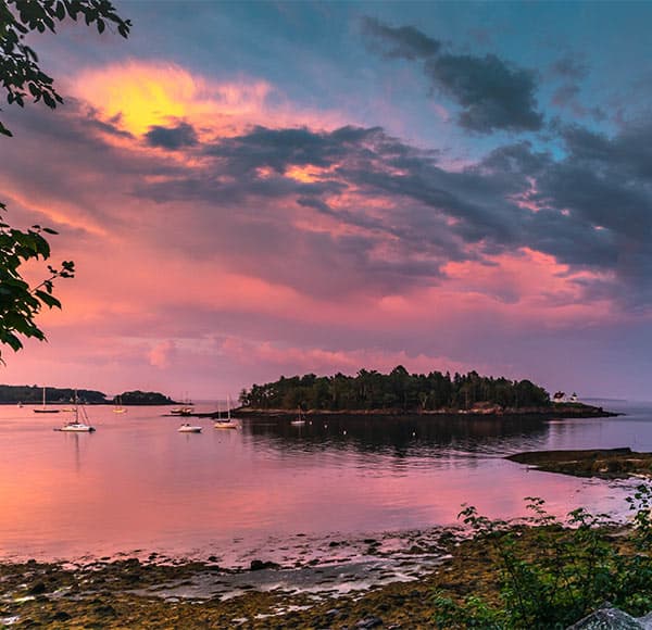 Sunset in Maine with sailboats and lighthouse in distance